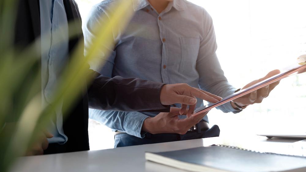 Businessmen holding a pen and analysis documents on office table with laptop computer and graph financial diagram working in the background